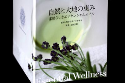 Book Essential Wellness top of image is cut off with Japanese lettering in the middle of the front cover, bleow that are flowers sitting on a towel with a glass, lower bottom displays that title Essential Wellness